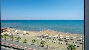 A beach with sun loungers and umbrellas, a clear sky, and the ocean. - Dinglis Beach Hotel Apartments (Larnaca)