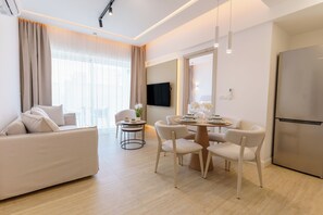 A modern living room with a sofa, dining table, chairs, and a flat-screen TV. - Dinglis Beach Hotel Suites (Larnaca)