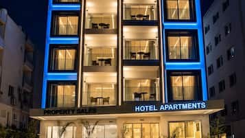 Un hotel de varios pisos con fachada moderna, balcones y un cartel que indica 'HOTEL APARTMENTS'.