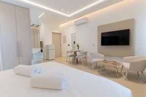 A modern hotel room with a large bed, a TV mounted on the wall, a desk with chairs, and a wardrobe. - Dinglis Beach Hotel Suites (Larnaca)