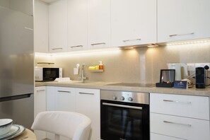 A modern kitchen with white cabinets, stainless steel appliances, and a coffee maker. - Dinglis Beach Hotel Suites (Larnaca)