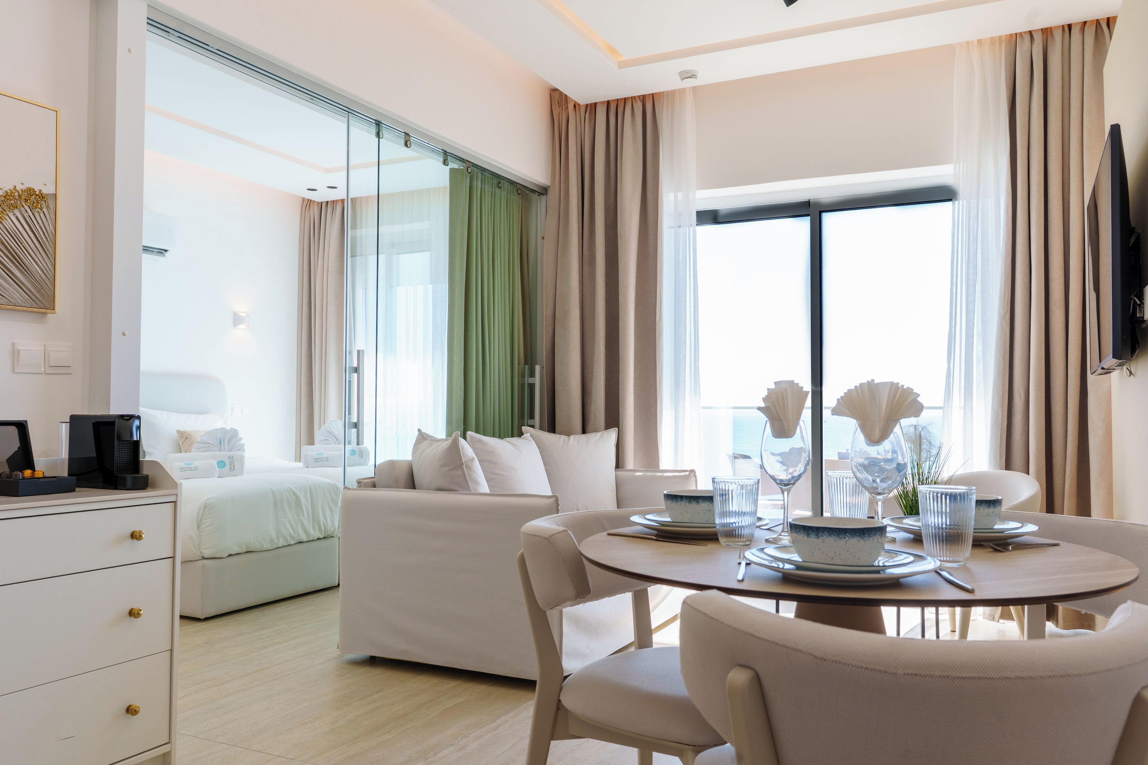 Habitación de hotel con cama, sofá, mesa de comedor con sillas y televisor montado en la pared.