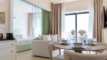 Habitación de hotel con cama, sofá, mesa de comedor con sillas y televisor montado en la pared.