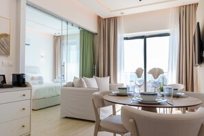 A hotel room with a bed, a sofa, a dining table with chairs, and a television mounted on the wall. - Dinglis Beach Hotel Suites (Larnaca)