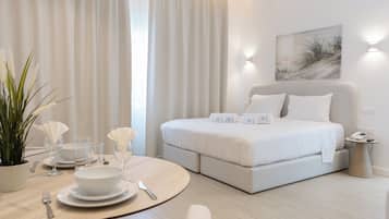 A modern hotel room with a bed, bedside table, and a dining area with a table set for two.