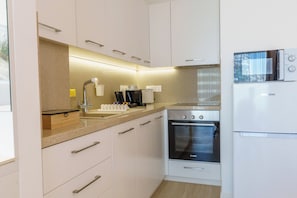 A modern kitchen with white cabinets, a stainless steel oven, a microwave, and a coffee maker. - Dinglis Beach Hotel Suites (Larnaca)