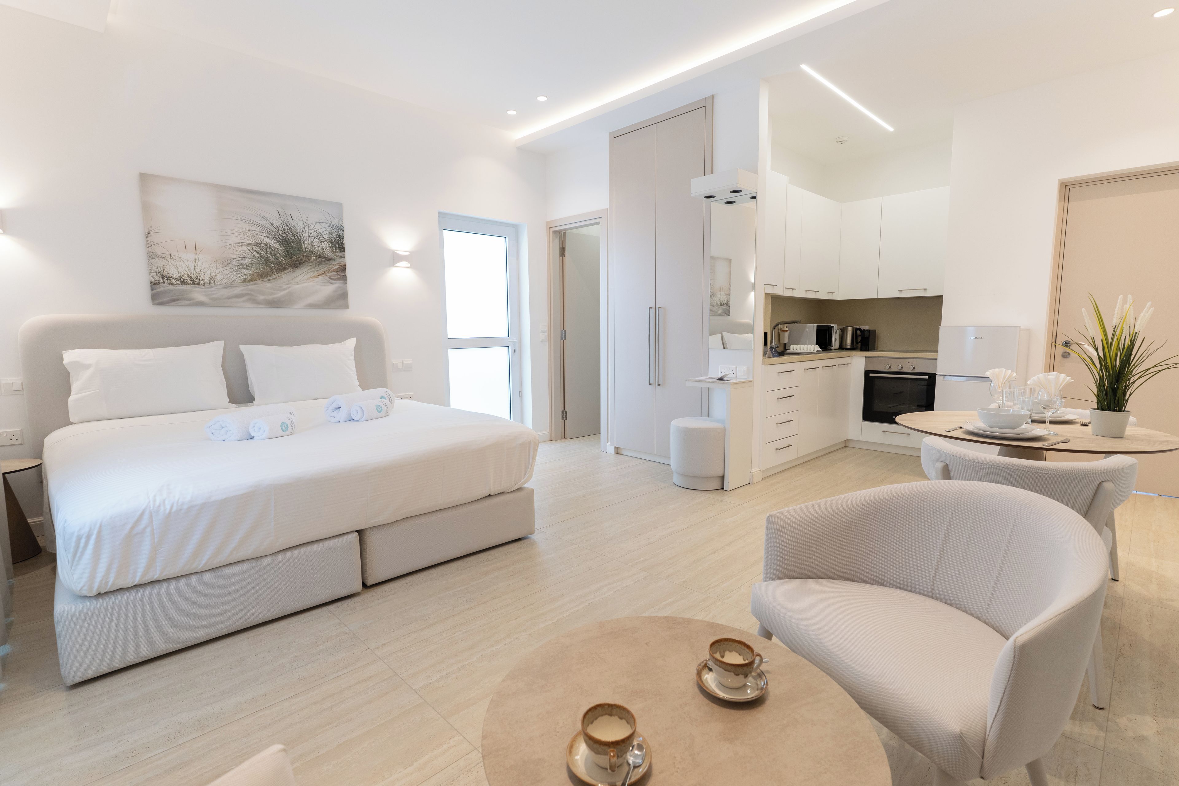 A modern hotel room with a large bed, a sitting area, and a kitchenette.