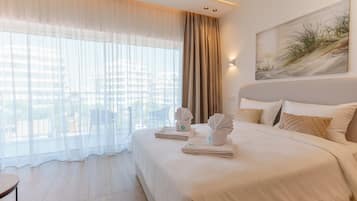 Habitación de hotel con una cama grande, vistas de la ciudad a través de cortinas translúcidas y un cuadro en la pared.