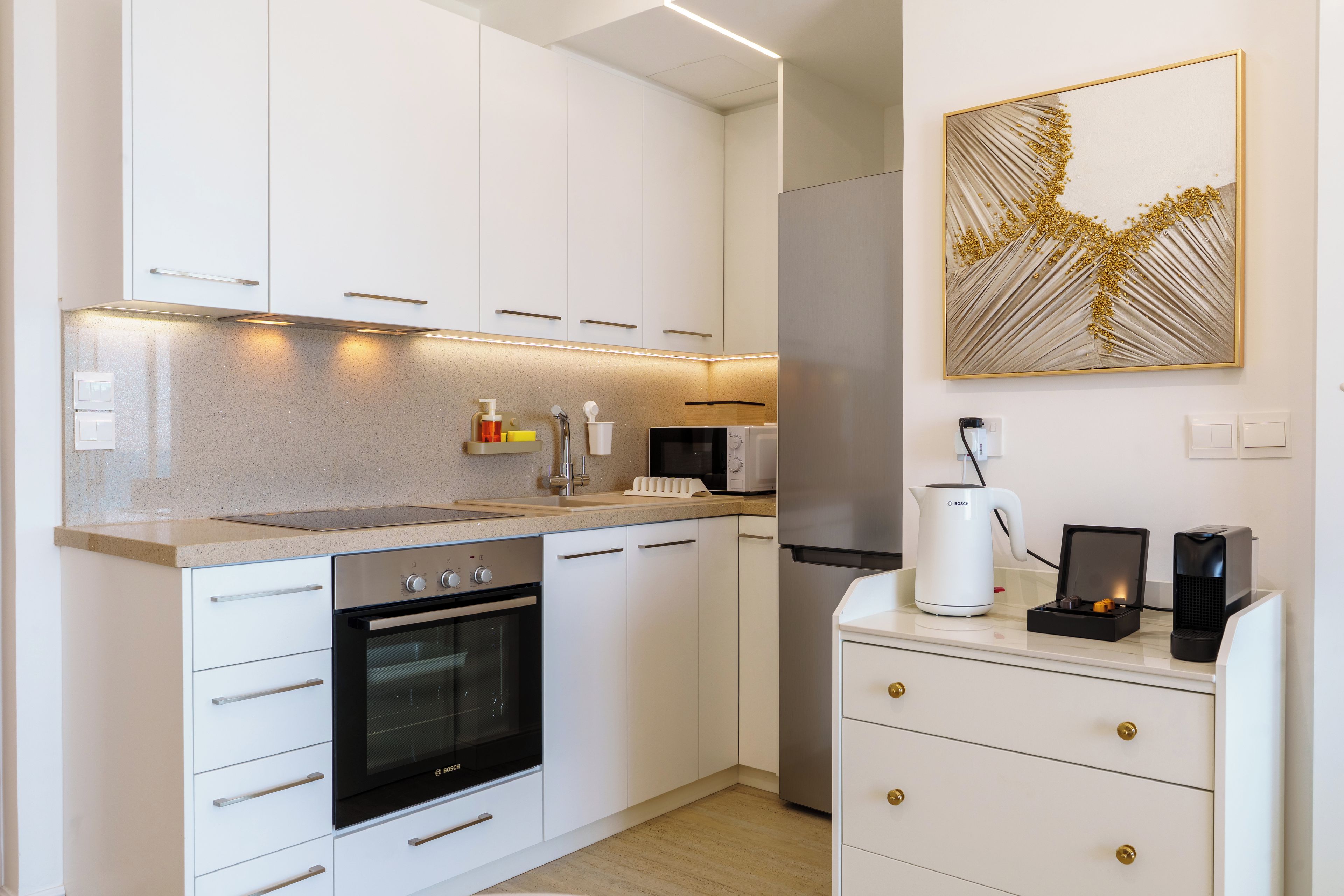 A modern kitchen with white cabinetry, a Bosch oven, a microwave, and a coffee machine.