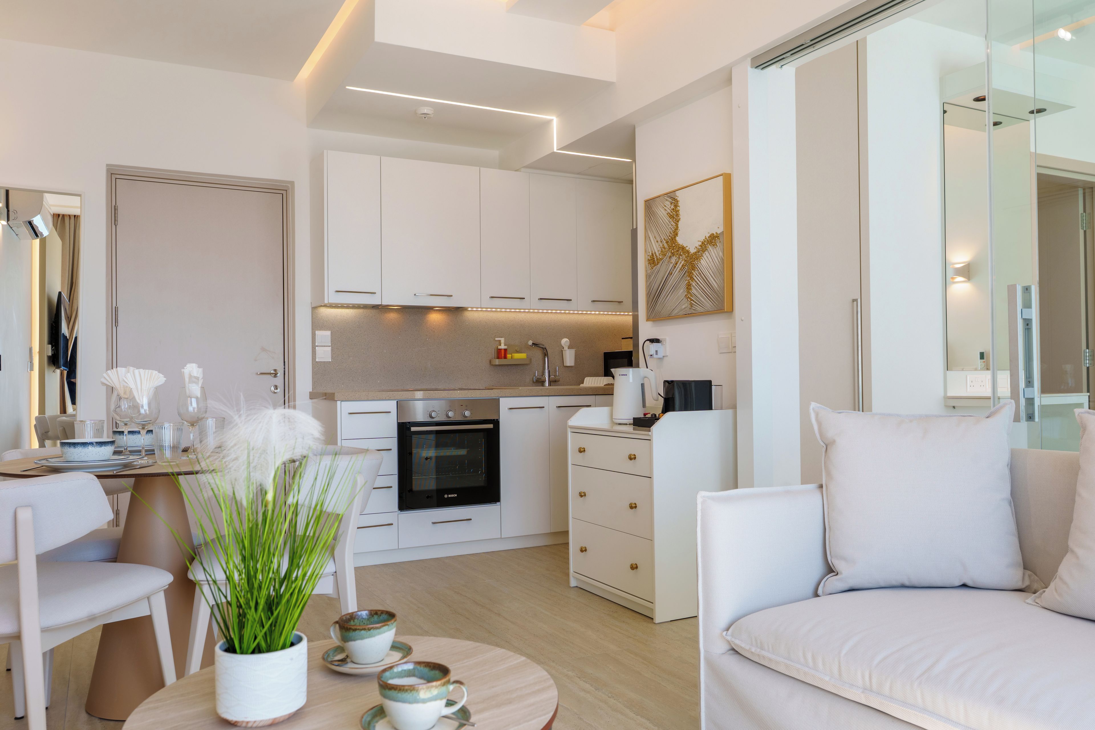Un salon moderne comprenant un canapé, une table à manger avec des chaises, un coin cuisine avec des placards et des appareils électroménagers, et un grand miroir.