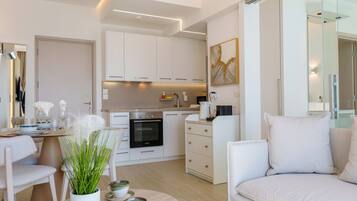 A modern living room with a sofa, a dining table with chairs, a kitchen area with cabinets and appliances, and a large mirror.
