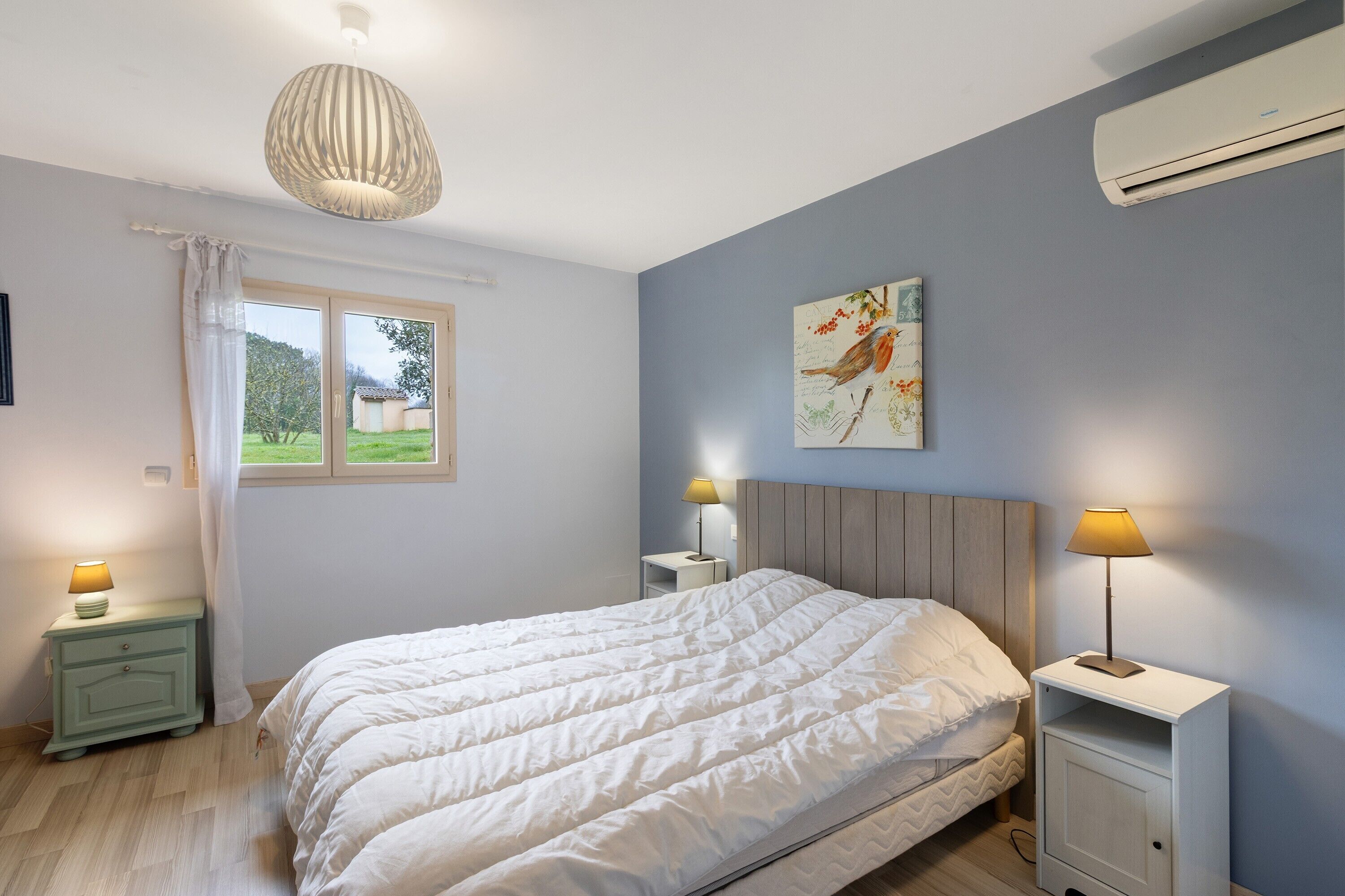 Quarto com cama, mesas de cabeceira, janela, ar-condicionado e luminária.