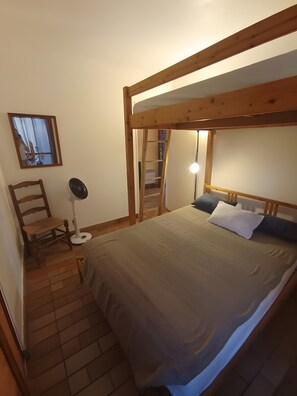 A bedroom with a bunk bed, a chair, a standing fan, and a mirror on the wall.