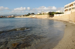 A coastal hotel with a beach view, clear water, and a rocky shoreline.
