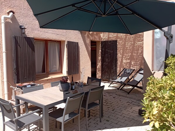 An outdoor patio with a table, chairs, an umbrella, and a potted plant.