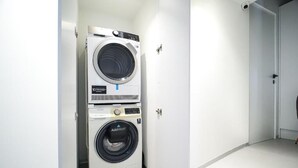 Ett kompakt, vitt tvättrum med en tvättmaskin och en torktumlare som man matar från framsidan, en dörr med ett handtag och ett kaklat golv.
