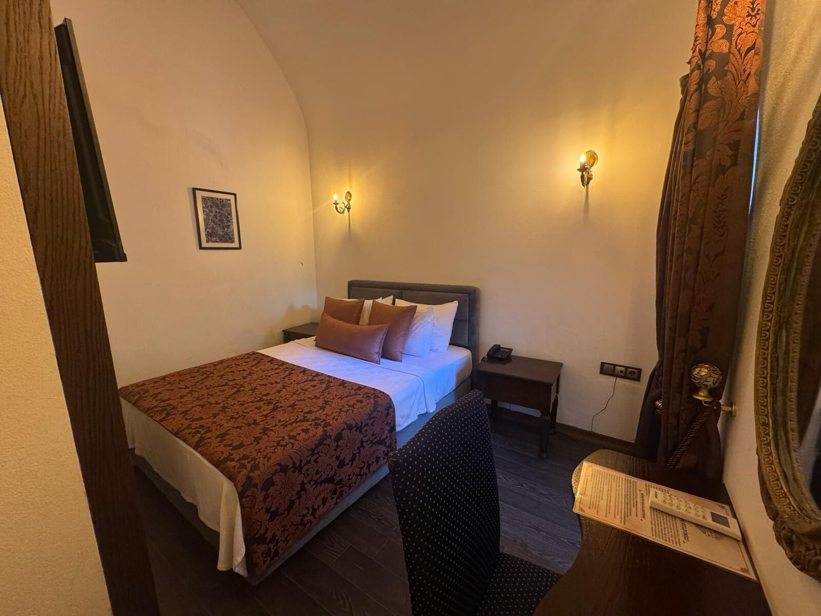 Un dormitorio con cama, mesitas de noche, una silla y un espejo.