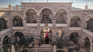 A courtyard with a central entrance, surrounded by multiple arches and balconies. Tables and chairs are arranged for outdoor dining. - Kervansaray Antique Hotel (Çeşme)