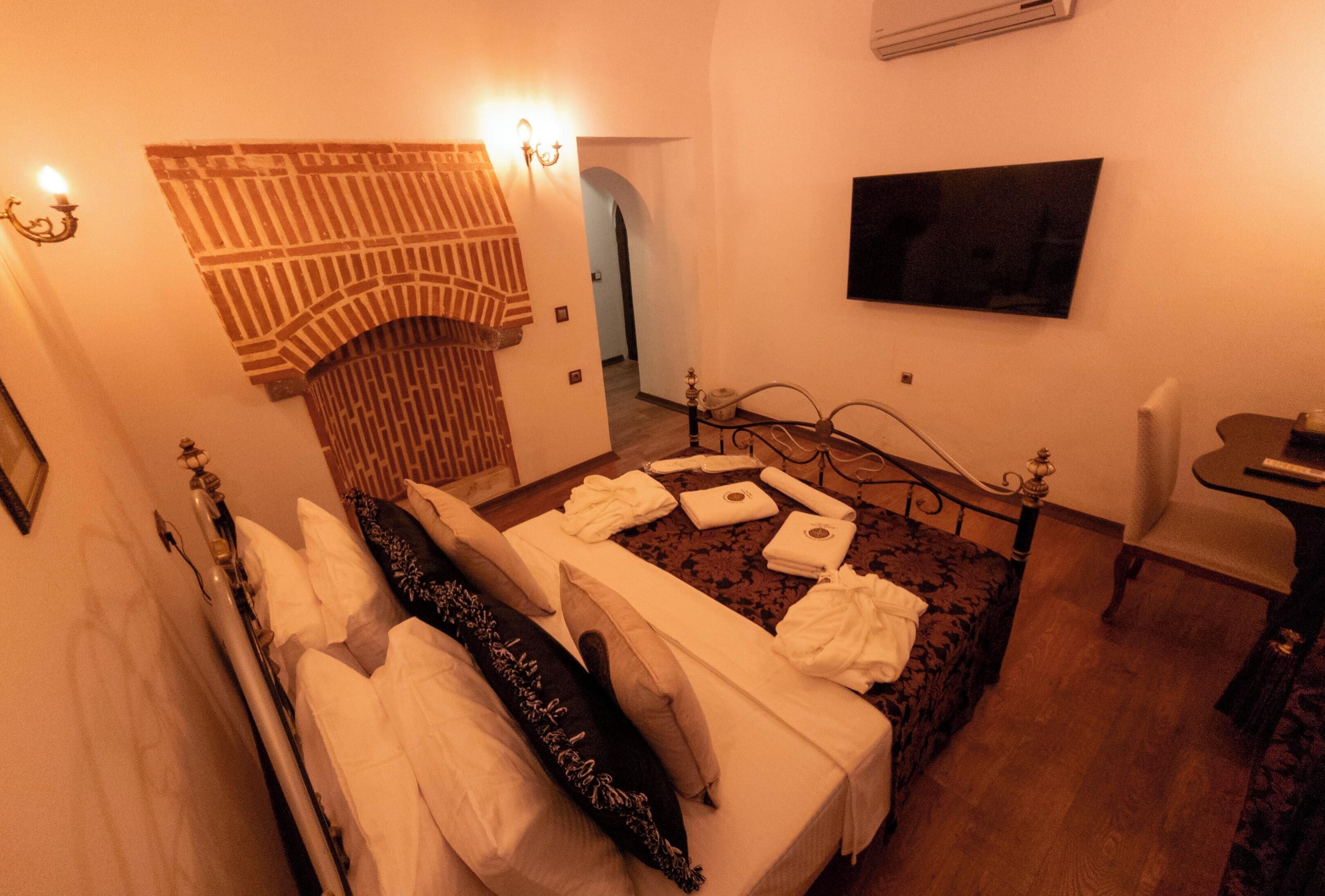 A hotel room with a bed, a TV, a chair, and a fireplace.