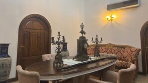 A room with a wooden table, chairs, a sofa, a chandelier, a clock, and a wall-mounted air conditioner. - Kervansaray Antique Hotel (Çeşme)
