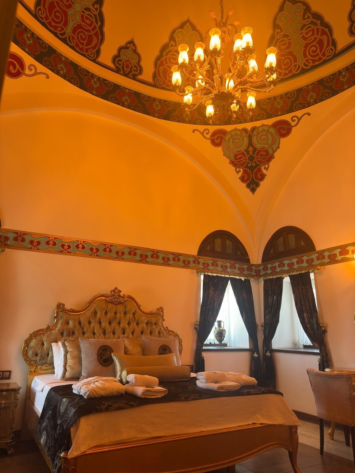 A room with a large bed, ornate ceiling, and a chandelier.