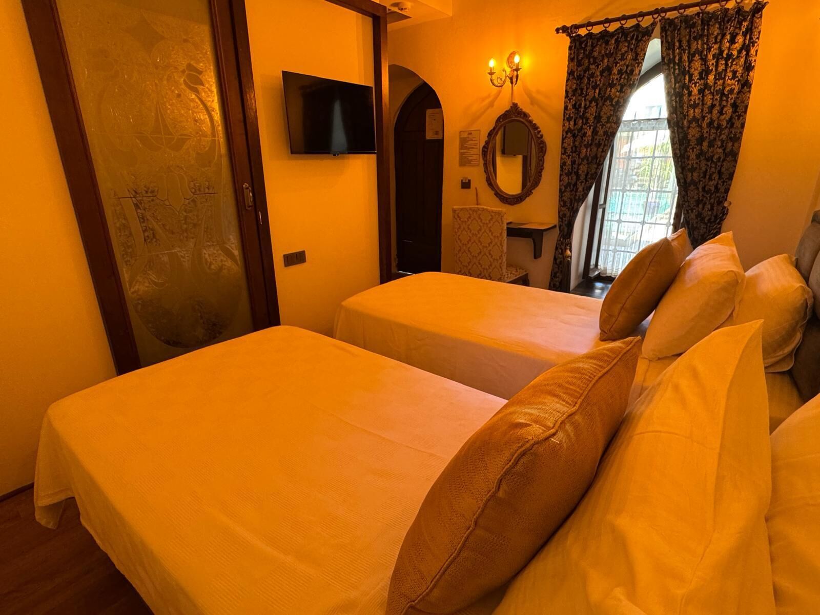 Quarto de hotel com duas camas, uma televisão, um espelho e uma janela com cortinas.