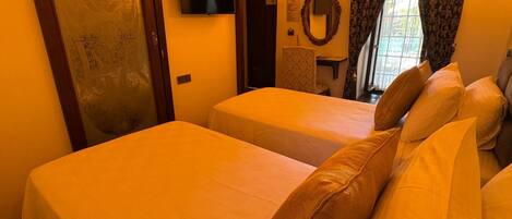 Quarto de hotel com duas camas, uma televisão, um espelho e uma janela com cortinas.