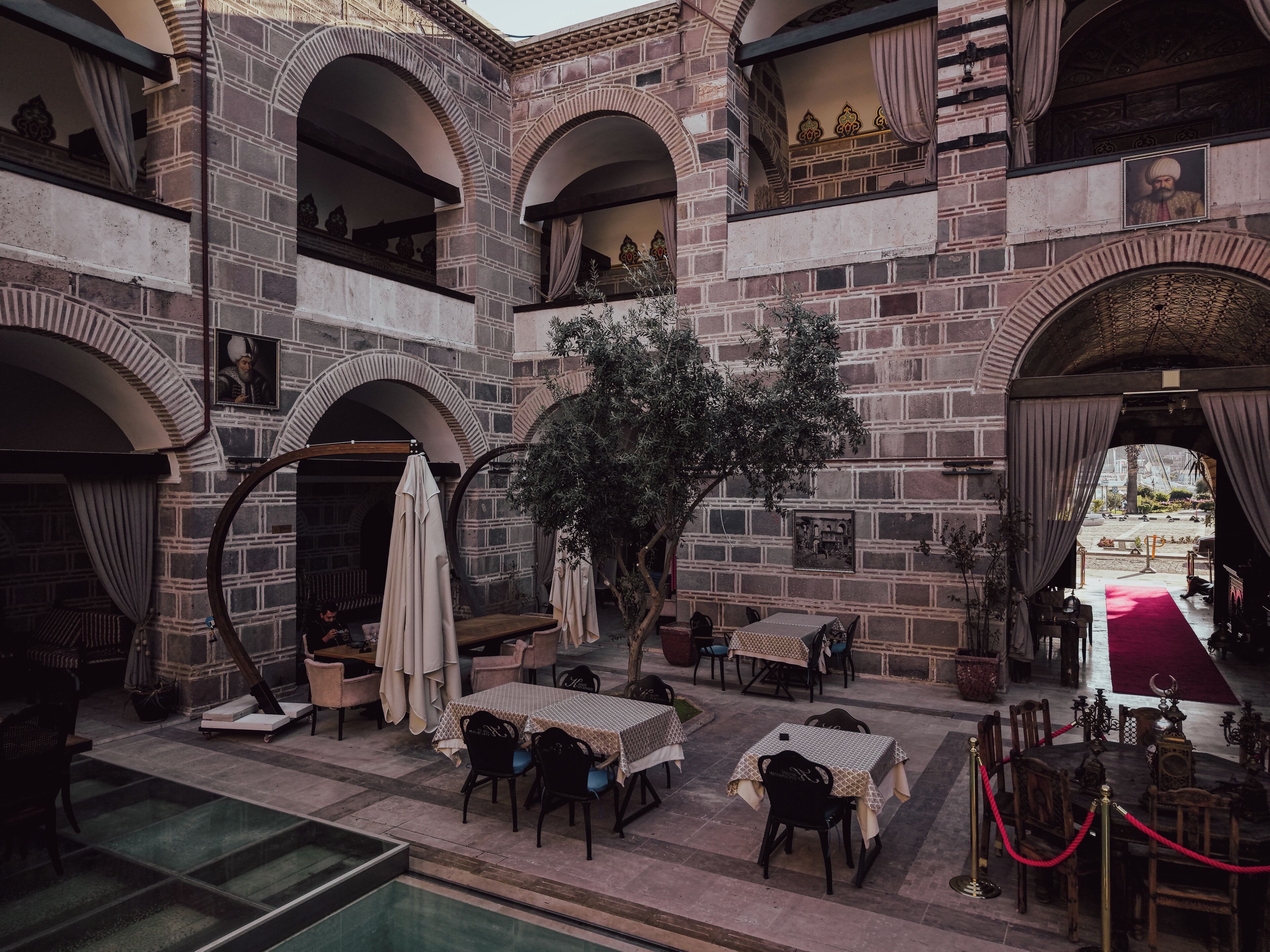 An indoor courtyard with stone arches, tables, chairs, and a red carpet leading to an entrance.