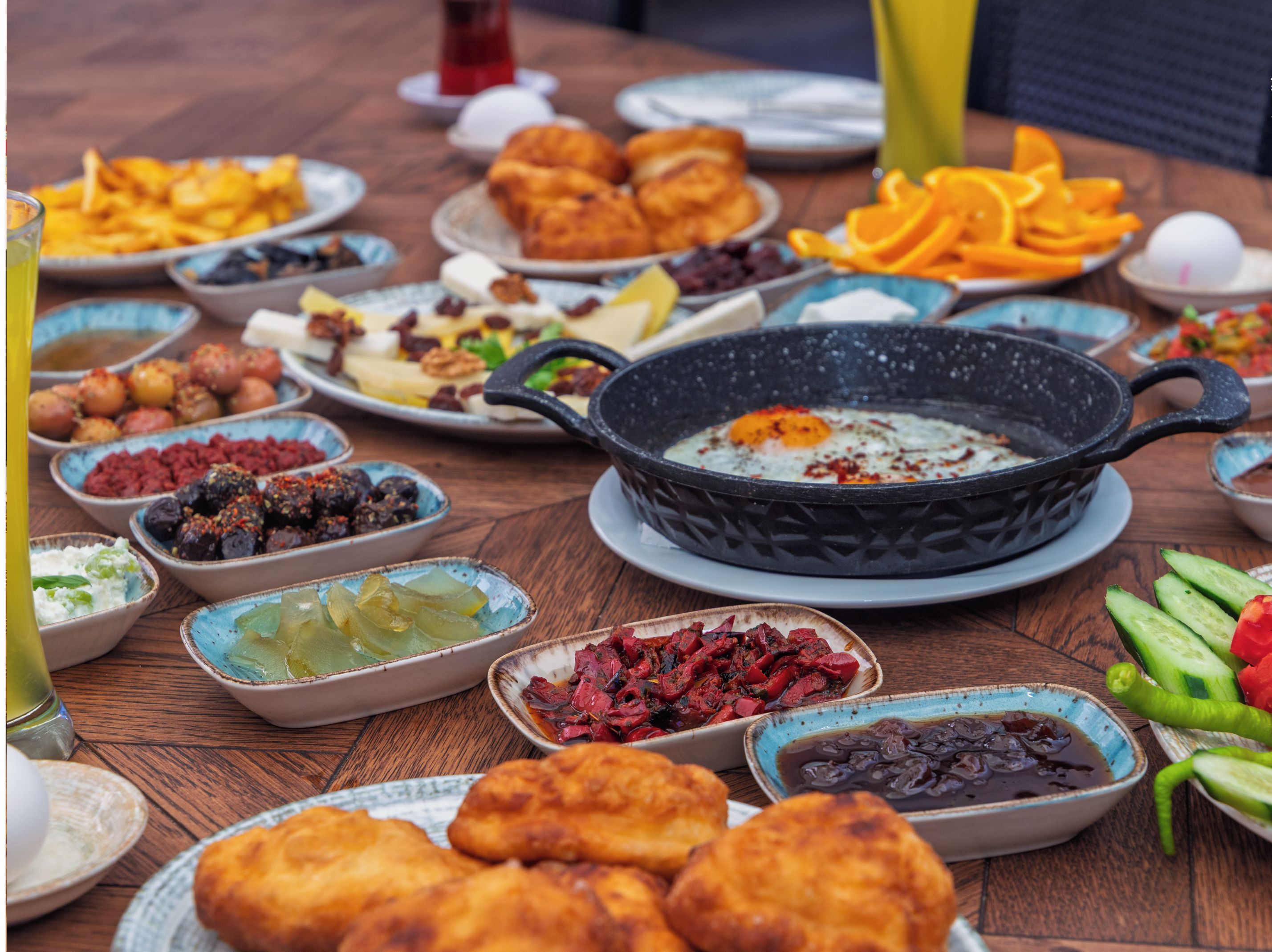 Variedad de platos sobre una mesa de madera, incluyendo una sartén negra con un huevo, cazos de salsas y platos de comida.