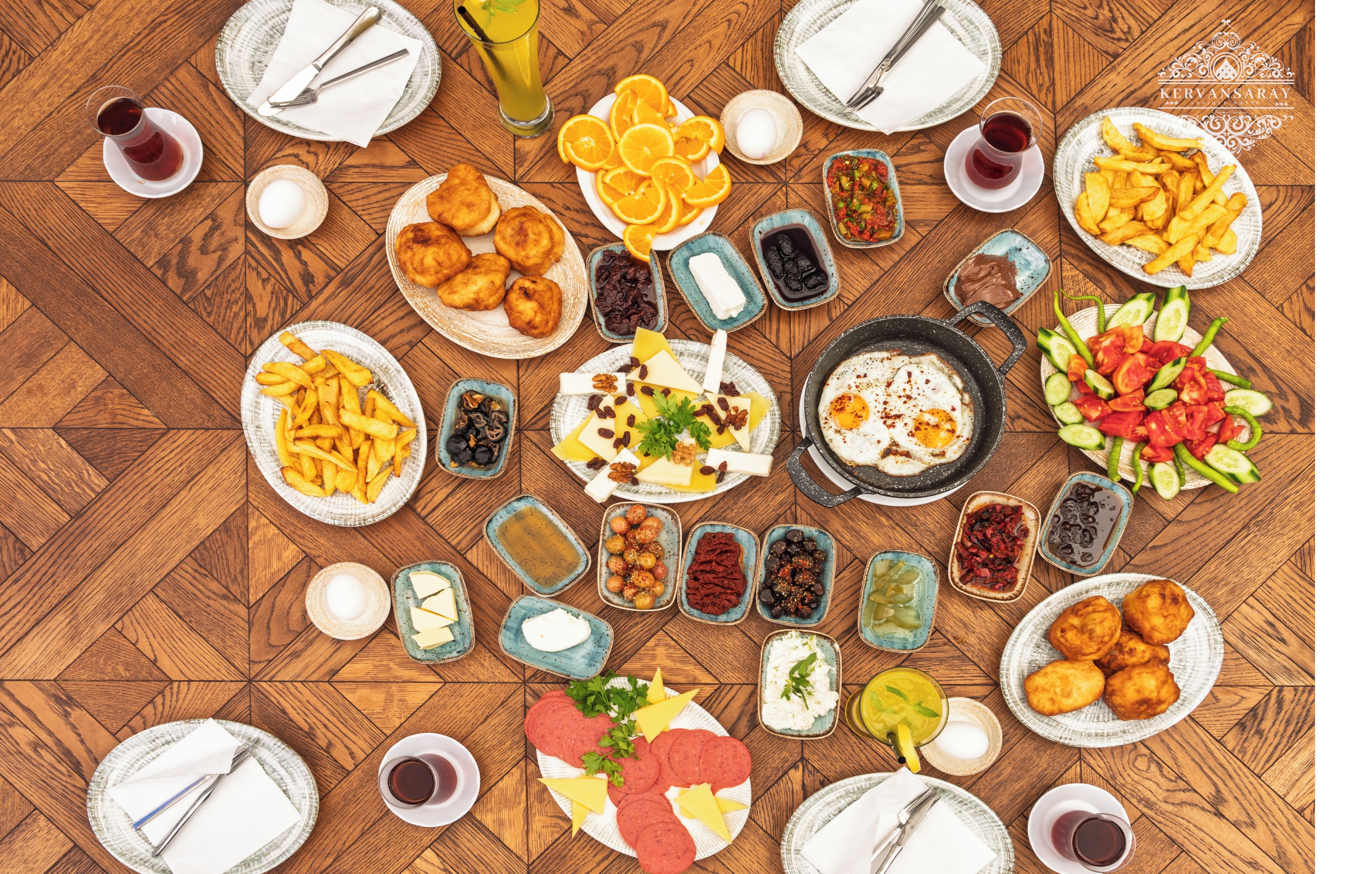 A wooden table with various dishes and drinks, including fried foods, fruits, and condiments.