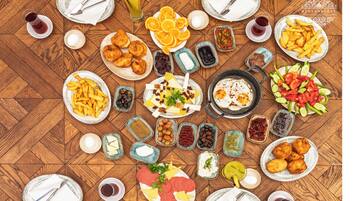 A wooden table with various dishes and drinks, including fried foods, fruits, and condiments.