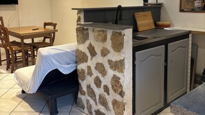 A compact kitchen with a stone backsplash, a dining area with a table and chairs, and a flat-screen TV mounted on the wall. - Apparently from the countryside (La Croix-sur-Ourcq)