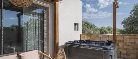 A modern outdoor seating area with a sofa, a hot tub, and a wicker lamp.