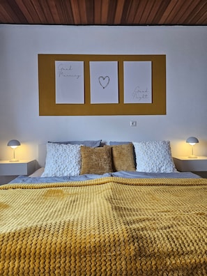 Une chambre à coucher comprenant un lit, deux tables de chevet, un tableau d’affichage fixé au mur avec trois notes, et une couverture à motifs.