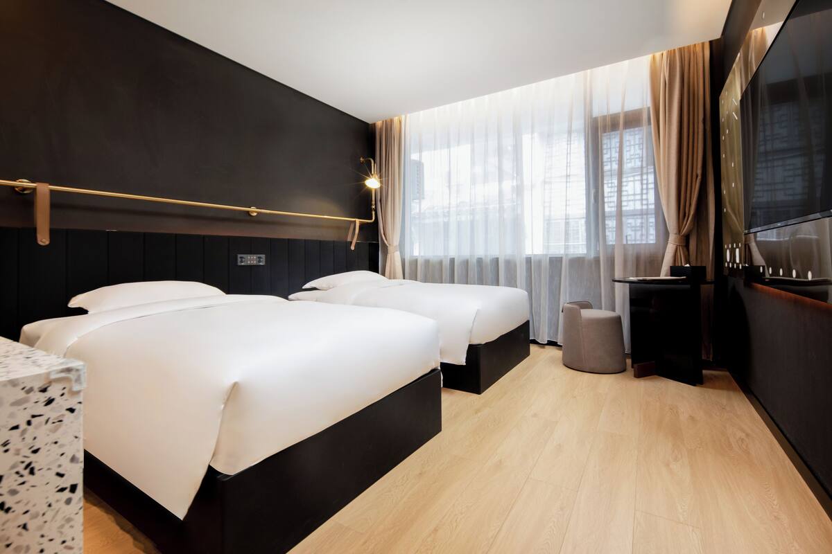 Una habitación de hotel moderna con dos camas, un escritorio y un televisor grande.