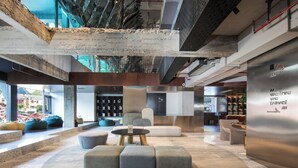 Eine moderne Lobby mit einer zentralen Sitzgruppe, einem Empfangsbereich und Blick auf die Stadt durch große Fenster.