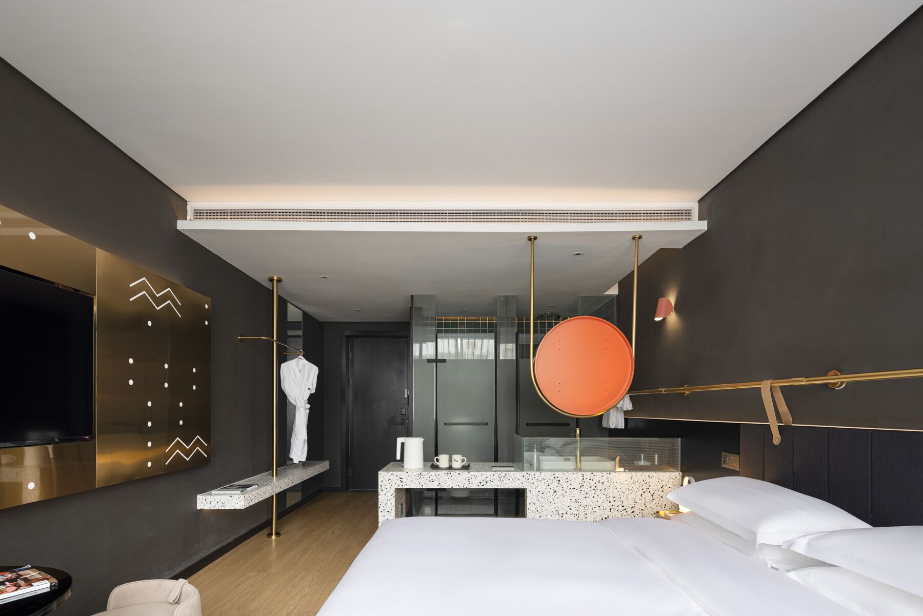 A modern hotel room with a large bed, a seating area with a small table, a TV mounted on the wall, and a large mirror.