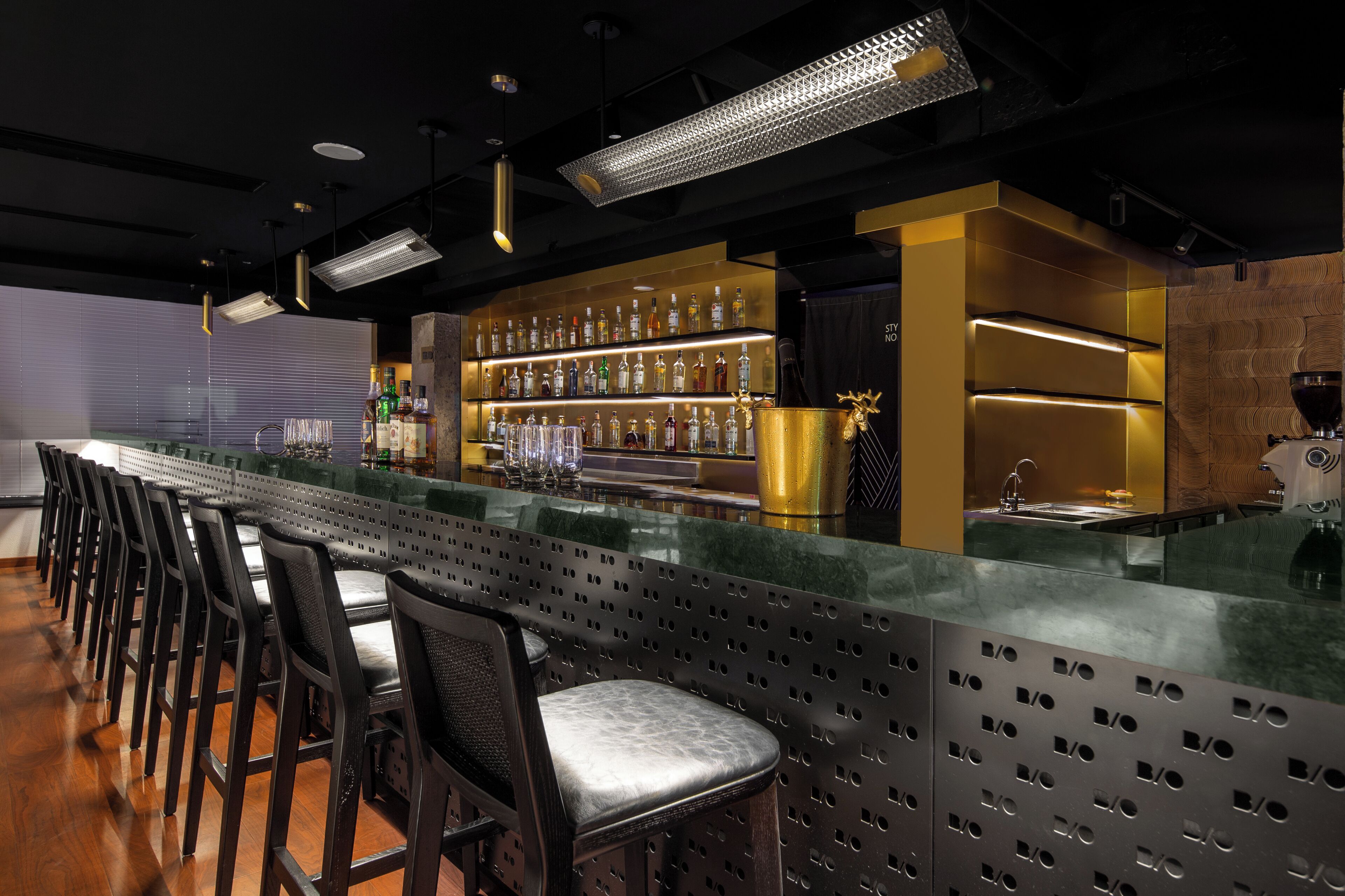 A bar area with a long counter, multiple shelves of bottles, and several chairs.
