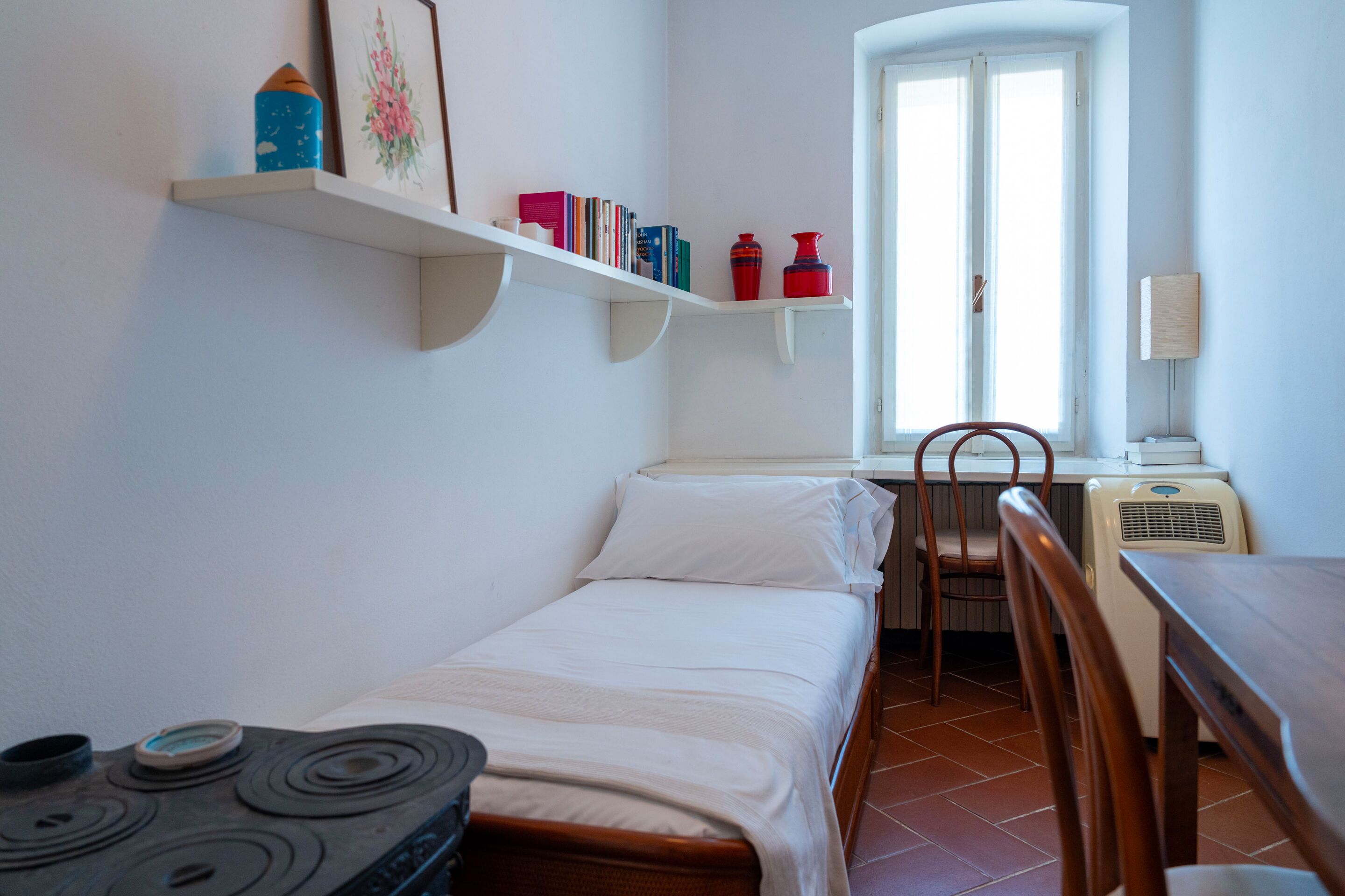 Ein kleines, ordentlich eingerichtetes Schlafzimmer mit Bett, Stuhl, Tisch und Fenster.