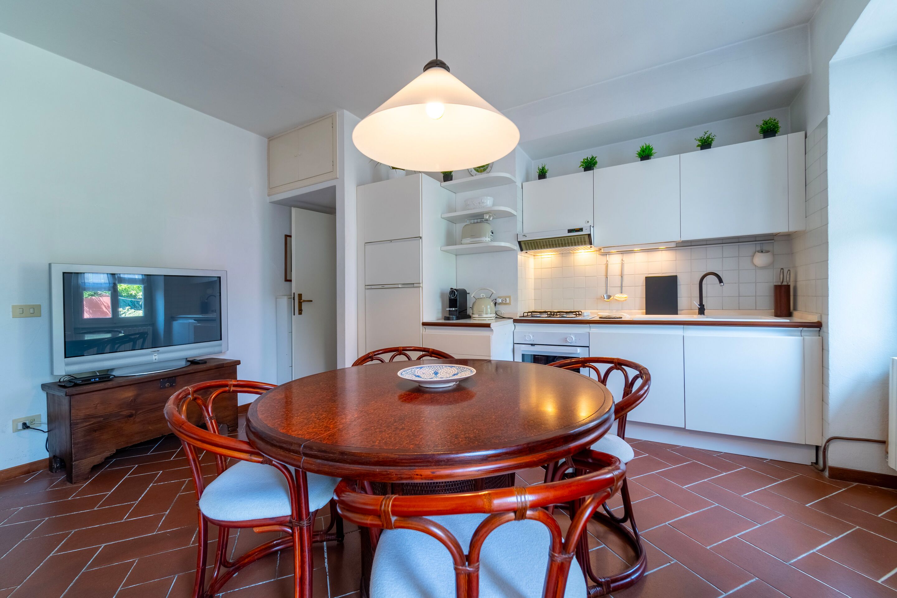Una cocina moderna con armarios blancos, una mesa de comedor con sillas y un televisor.
