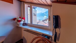 Une pièce avec un plafond en bois, une fenêtre donnant sur une montagne et un dôme, un radiateur, un fauteuil en osier et un téléphone.