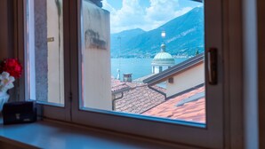 Une vue par la fenêtre sur une ville côtière, avec un imposant dôme en évidence, une montagne en arrière-plan et une étendue d'eau.
