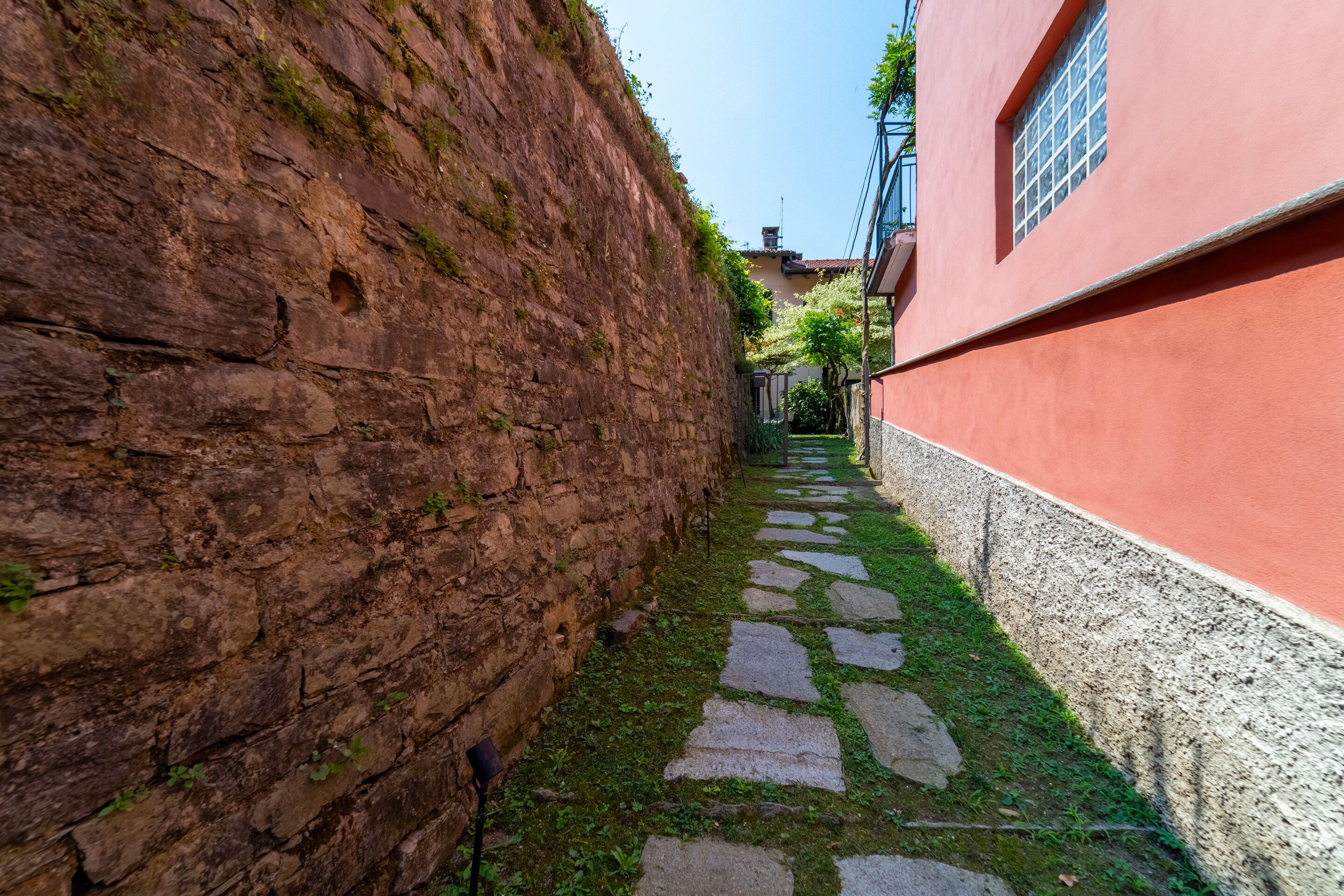 Une ruelle étroite pavée de pierres, un mur de briques d’un côté et un bâtiment à la façade rouge et aux fenêtres de l’autre.