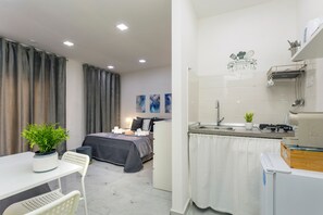 A compact room with a bed, bedside table, and a small dining area.