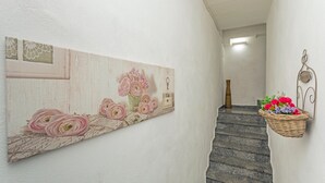 Un pasillo con un cuadro decorativo, una cesta de mimbre con flores y una escalera.