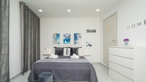 Un dormitorio moderno con cama, cortinas grises, un aparador y obras de arte en la pared.