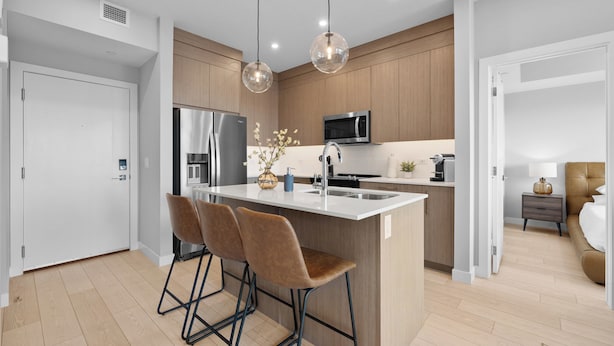 Una cocina moderna con una isla central, taburetes de bar, un microondas y un fregadero.
