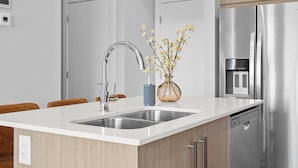 Una cocina moderna con un refrigerador de acero inoxidable, un lavavajillas empotrado, un lavamanos doble y un jarrón con flores amarillas.