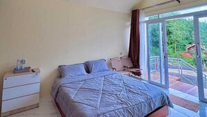 Un dormitorio con una cama grande, una mesita de noche, una silla y vistas al exterior a través de una puerta corredera.