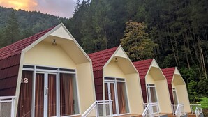 Una hilera de cabañas de tres pisos con techos rojos, barandas blancas y un área verde al frente.